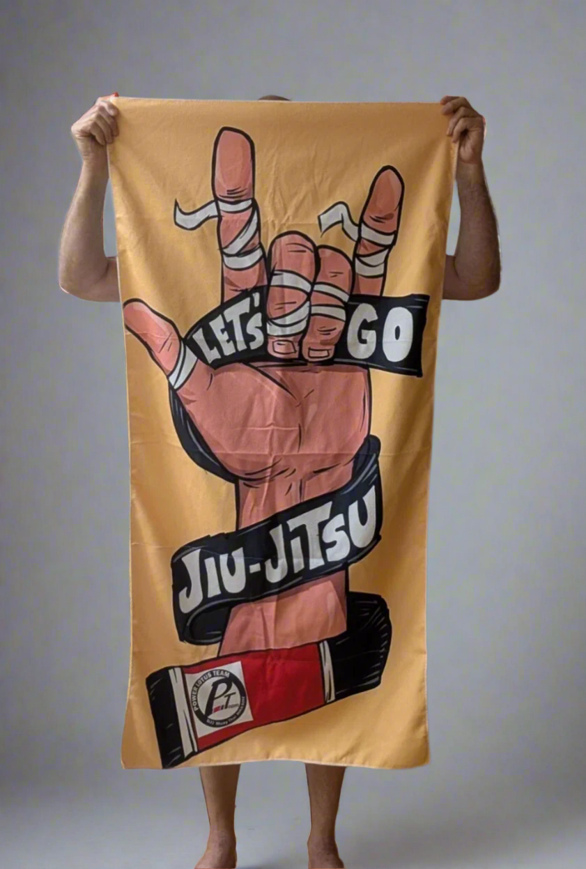 Person holding a yellow towel with a Jiu-Jitsu design against a plain wall.