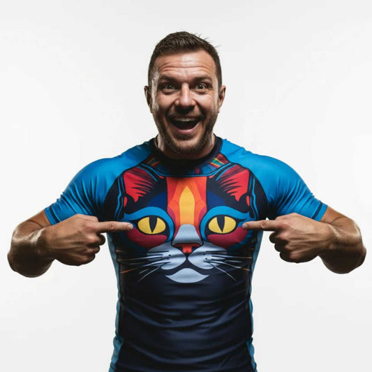 Man wearing a blue BJJ rash guard  with a colorful cat design, pointing at the shirt.