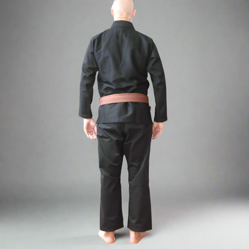 Person wearing a black jiu jitsu gi with a brown belt on a white background, featuring the Janners BJJ logo.