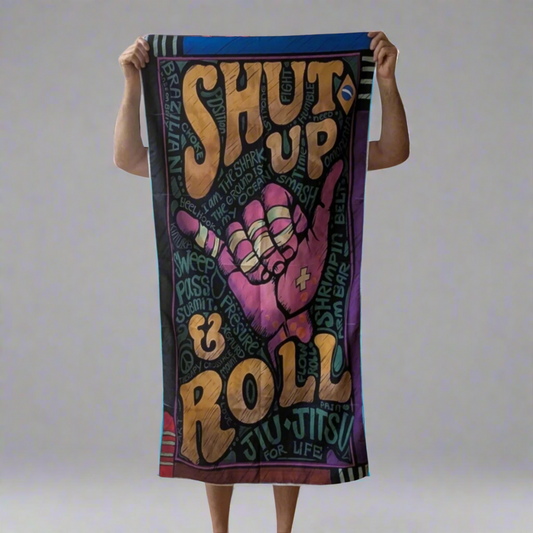 Towel with 'Shut Up & Roll Jiu Jitsu For Life' text and graphic design held by a person.