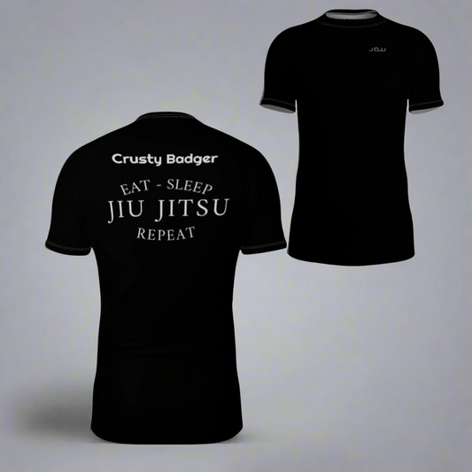 Black rash guard with 'Crusty Badger' and 'Eat - Sleep Jiu Jitsu Repeat' text on a white background